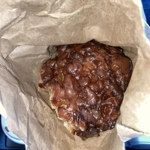 a chocolate covered donut in a brown paper bag