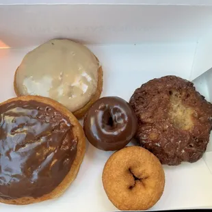 Assortment of donuts: chocolate cinnamon roll, maple cinnamon roll, chocolate cake, plain cake, and apple fritter