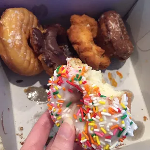 a hand holding a donut with sprinkles