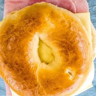 a hand holding a bagel with ham and cheese