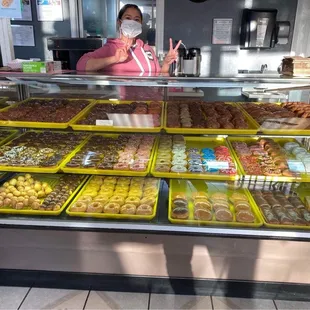 a woman wearing a face mask behind a display case of donuts