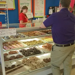 a man standing in front of a display case of doughnuts