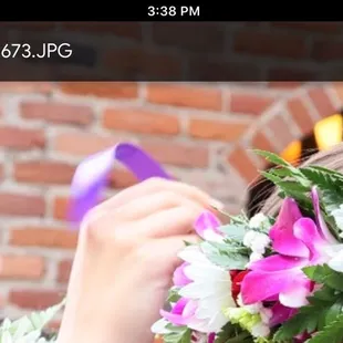 Flowers and greenery shown as a hand ties the haku lei ribbon around somebody's head.