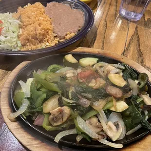 Sizzling vegetarian fajitas with beans, rice, and tortillas on the side.