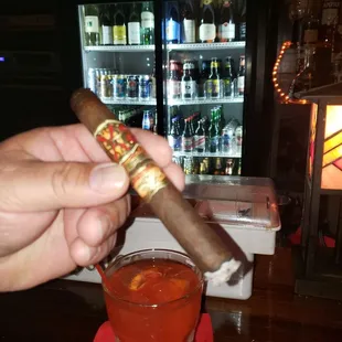 a hand holding a cigar and a glass of alcohol