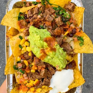 a hand holding a tray of nachos