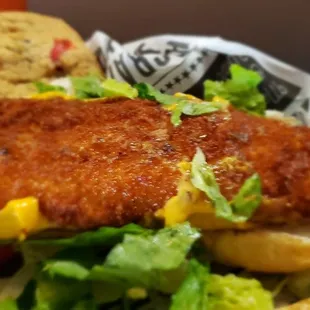 a fish sandwich with lettuce, corn, and pickles