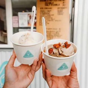 two hands holding two cups of ice cream