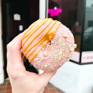 a hand holding a pink donut with caramel drizzle