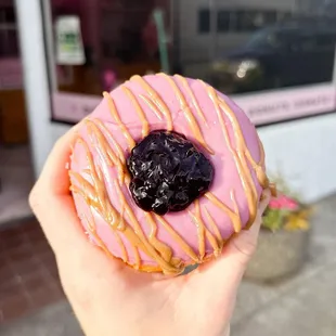 a hand holding a pink donut with blueberry filling