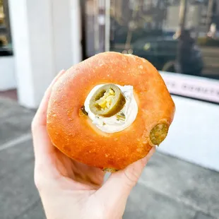 a hand holding a donut with cream and jalapenos