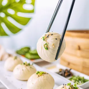 a person holding chopsticks over a row of dumplings