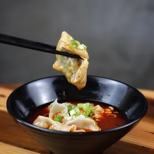 a black bowl with dumpling and chopsticks