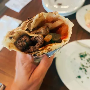 Inside 26. Shawarma Beef. Has meet, pickles, tomatoes, and onions.