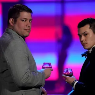 two men dressed in tuxedo, one holding a wine glass