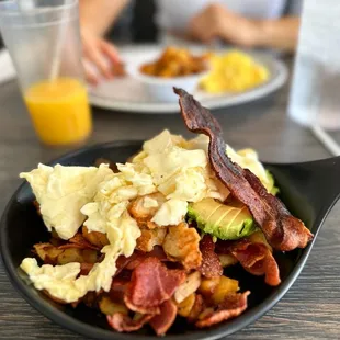 a plate of bacon, eggs, avocado, and hash browns