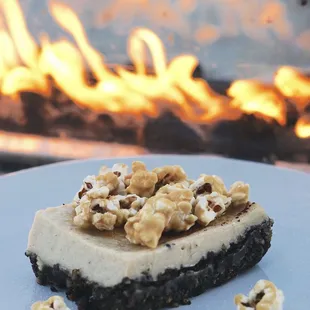 a slice of cheesecake on a plate in front of a fire