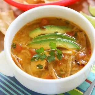 a bowl of soup with tortilla and avocado