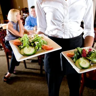 a waitress holding two plates of salads