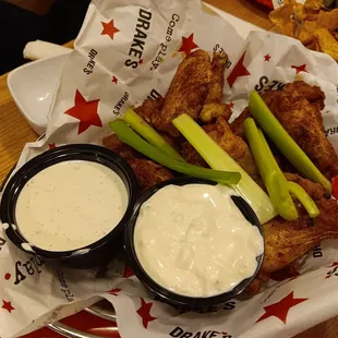a basket of chicken wings with dips and celery