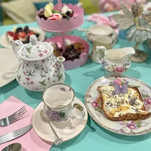 a little girl sitting at a table with a tea set