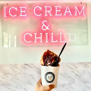 a hand holding a cup of ice cream and chill
