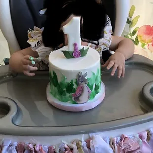 a young girl sitting in a highchair with a birthday cake