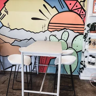 a table and chairs in front of a colorful mural