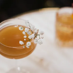 a cocktail in a coupe glass with baby's breath