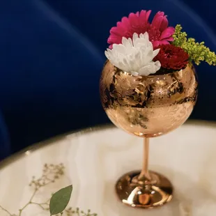a gold wine glass with flowers in it