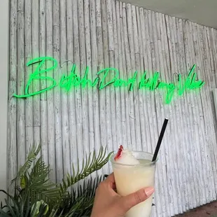 a hand holding a drink in front of a neon sign