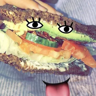 Avocado sandwich on pumpernickel with bacon and veggies.