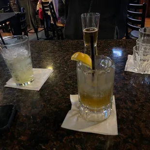a man sitting at a table with two glasses of alcohol and a lemon wedge