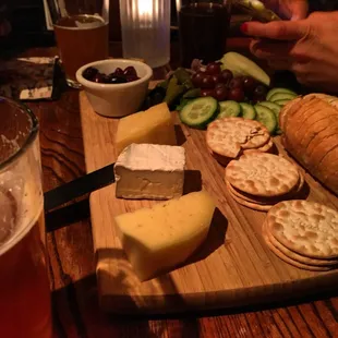 a cheese board with crackers, grapes, cucumbers, and bread