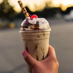 a hand holding a cup of ice cream with a cherry on top