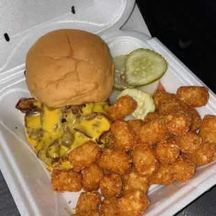 a burger and tater tots in a styrofoam container