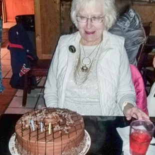 an elderly woman cutting a chocolate cake