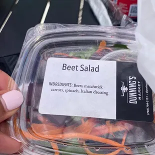 a hand holding a container of beef salad