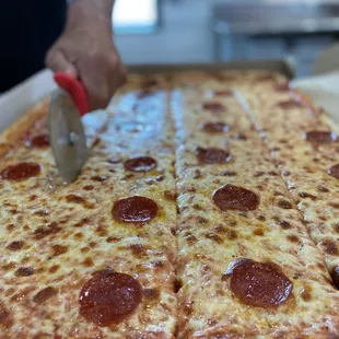 a person cutting a pepperoni pizza