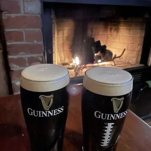 two pints of guinness in front of a fireplace