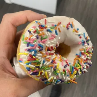 a hand holding a frosted donut with sprinkles