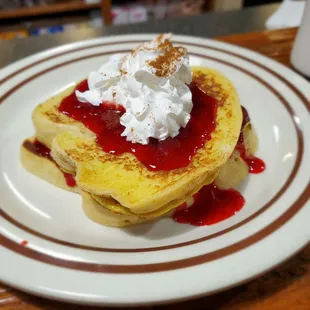 Stuffed French toast with strawberry topping and whip cream dusted with cinnamon.