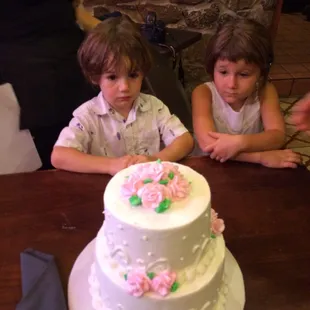 two children sitting at a table with a cake in front of them
