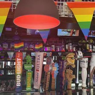 a row of beer taps with a rainbow flag in the background