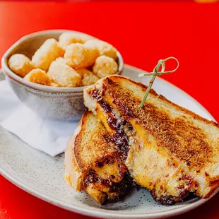 a grilled cheese sandwich on a plate with a bowl of tater tots