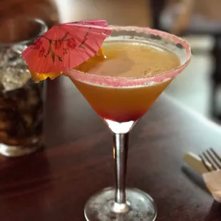 a cocktail in a martini glass with a pink umbrella