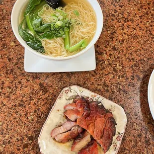 a bowl of noodles, a plate of meat, and a bowl of broccoli