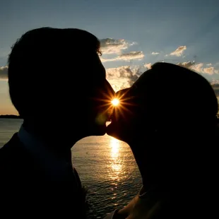 a silhouette of a bride and groom kissing at sunset