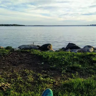 a person's feet resting on the grass near a body of water