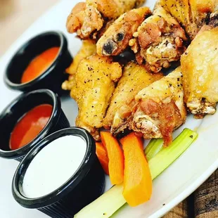 a plate of chicken wings with dipping sauces